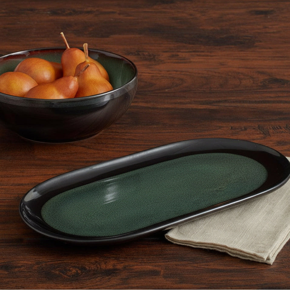Three croissants on a dark green plate with a bowl of pears in the background on a wooden table.